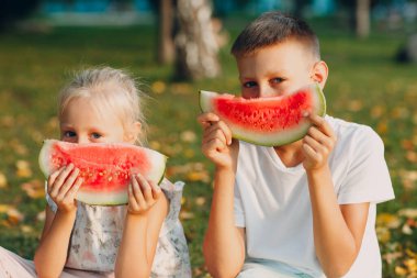 Küçük tatlı çocuklara sonbahar parkındaki çayırda sulu karpuz yiyen küçük kız ve oğlanlara