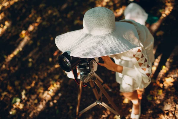 Wanita muda fotografer dengan gaun putih dan topi dengan kamera di musim gugur taman. — Stok Foto
