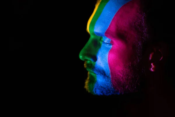 Rainbow Flag on face of adult man in dark.