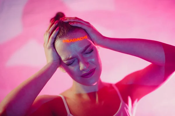 Молодая взрослая женщина держит руки на голове объявление с страданием выражения лица со словом головная боль на лице — стоковое фото