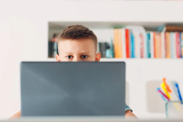 Νεαρό αγόρι κάθεται στο τραπέζι με φορητό υπολογιστή και ετοιμάζεται για το σχολείο. Έννοια ηλεκτρονικής εκπαίδευσης. — Φωτογραφία Αρχείου