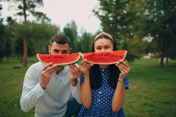 Młoda dorosła kobieta i mężczyzna para piknik na zielonej trawie łąka w parku zabawy i uśmiech z arbuzem — Zdjęcie stockowe