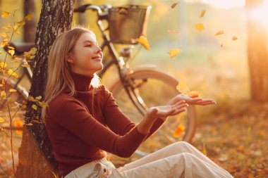 Günbatımında sonbahar parkında bisiklet süren mutlu, aktif genç bir kadın.
