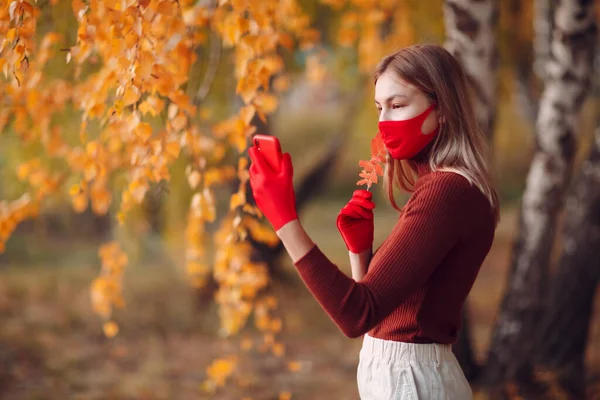 Aktive junge Frau in roten Handschuhen und Gesichtsmaske im Herbstpark mit Handy — Stockfoto