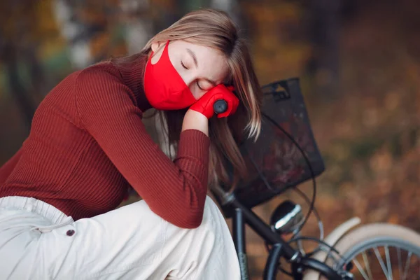 Jonge vrouw op de fiets met rode handschoenen en gezichtsmasker in het herfstpark — Stockfoto