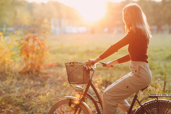 Feliz jovem ativo andando de bicicleta vintage com cesta no parque de outono ao pôr do sol — Fotografia de Stock