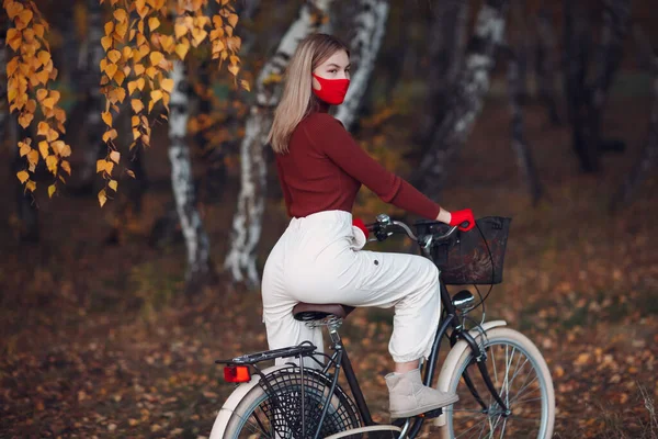 Young woman riding bicycle in red gloves and face mask at autumn park — Stock Photo, Image