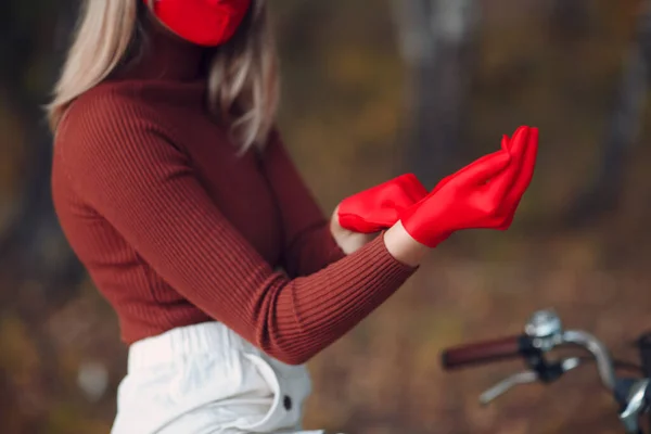 Jovem mulher andando de bicicleta e colocar luvas vermelhas e máscara facial no parque de outono — Fotografia de Stock