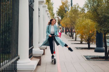 Genç bir kadın şehirde elektrikli scooter kullanıyor.