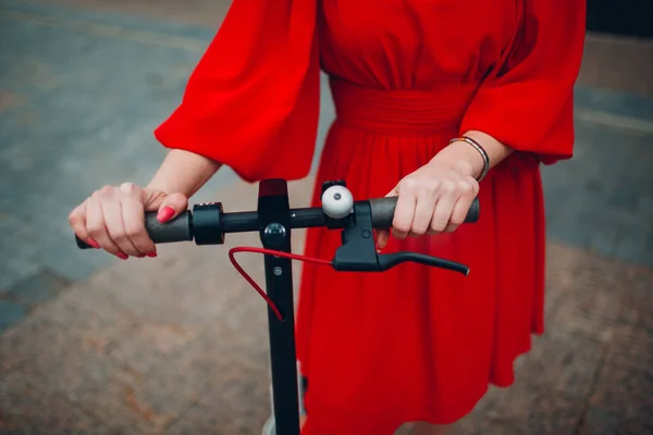 Jovem mulher detém volante de scooter elétrico em vestido vermelho na cidade — Fotografia de Stock