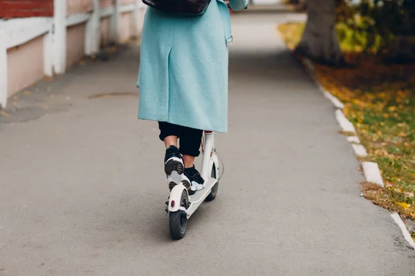 Giovane donna con scooter elettrico in cappotto blu in città — Foto Stock