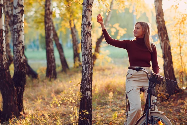 Feliz jovem ativo montando bicicleta vintage no parque de outono ao pôr-do-sol — Fotografia de Stock