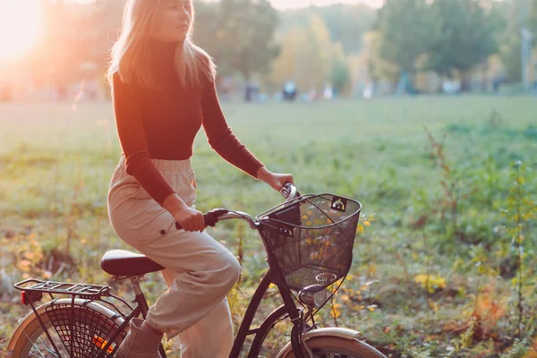 Feliz jovem ativo andando de bicicleta vintage com cesta no parque de outono ao pôr do sol — Fotografia de Stock