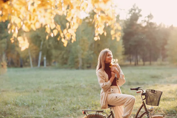 Happy active młoda kobieta trzyma jesień liści w ręcznej jazdy na rowerze w jesiennym parku — Zdjęcie stockowe