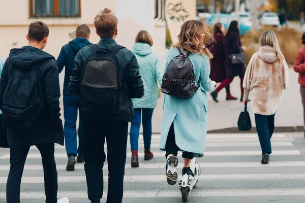 Jonge vrouw met elektrische scooter in blauwe jas op de oversteekplaats verkeersweg op de stad — Stockfoto