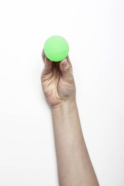 Kadın eli beyaz masada yeşil lastik bir top tutuyor..