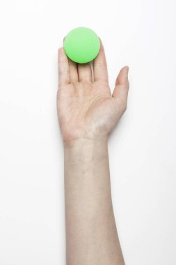 Kadın eli beyaz masada yeşil lastik bir top tutuyor..
