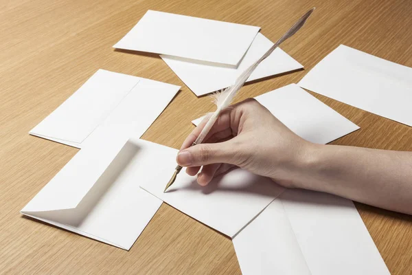 woman hand hold a feather quill pen with envelope, letter on the wood table,