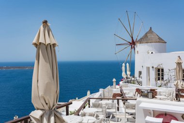 Tabkes, sandalye ve Santorini, Yunanistan köyde Oia üzerine katlanmış şemsiye ile yel değirmeni