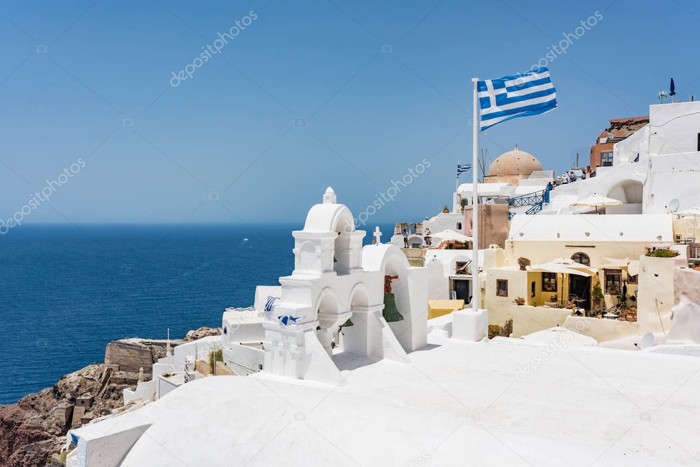 Green bells and flacg of Greece on roof of the church in the Oia village at Santorini, Greece.