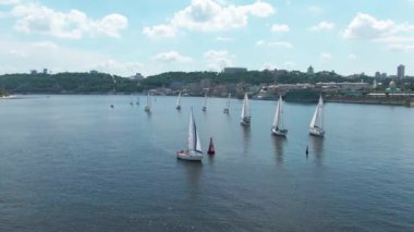 Yelkenli Yat şamandıra dönüyor. Nehirde yat yarışı. Şehir merkezinde yeşil ağaçlar ve evlerin önünde. Yolda bir sürü araba var. Bulutlu yaz gökyüzü. 4k hava drone görüntüleri.