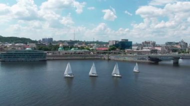 Yatlar nehirde yelken açin. Önde hızlı araba ile şehir. Beyaz gemilerle yelken yarışı. Yaz aylarında bulutlu gökyüzü. 4k hava drone görüntüleri.