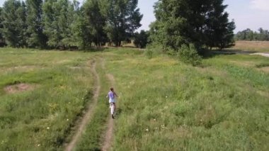 Ağaçlara doğru giden yeşil alanda bisiklet süren güzel genç bir kadın..