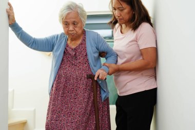 Bakıcı hastanede tekerlekli sandalyede oturan Asyalı yaşlı kadın maluliyet hastasına yardım ediyor..