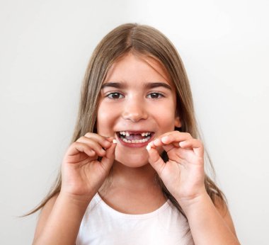 Gülümseyen, kameraya bakıyor ve diş elinde tutan küçük kız 