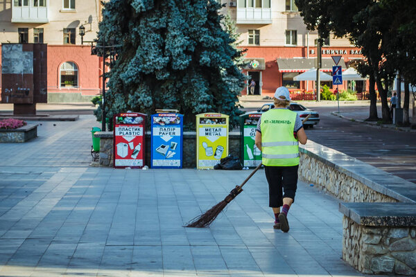 Zhytomyr, Ukraine - August 4, 2018: The Janitor cleans the city. Separation of garbage. A woman janitor sweeping the park for cleanliness and order on a sunny day.