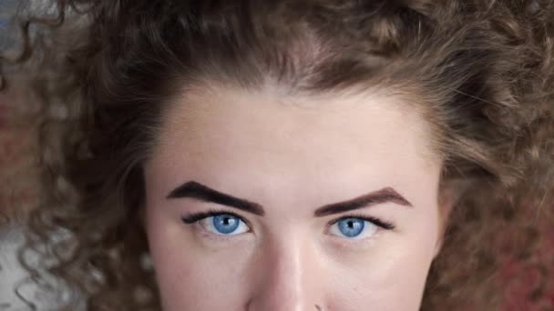 Video portrait of curly woman that opes her blue eyes and smiles, attractive woman with piercing in her nose, woman with big blue eyes — Stock Video