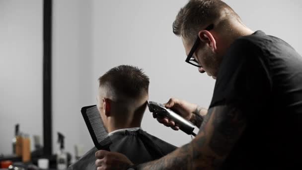 Peluquero tatuado hace corte de pelo para el cliente en la peluquería mediante el uso de peluquero, corte de pelo mans y afeitarse en la peluquería, peluquería y salón de afeitar — Vídeos de Stock