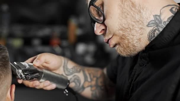 Татуйований перукар робить зачіску для клієнта в перукарні, використовуючи зачіску, чоловічу зачіску та гоління в перукарні, перукарню та гоління салону — стокове відео