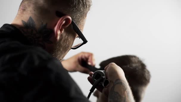 Le coiffeur tatoué fait une coupe de cheveux pour le client au salon de coiffure en utilisant une tondeuse, une coupe de cheveux et un rasage au salon de coiffure, au salon de coiffure et au salon de rasage. — Video