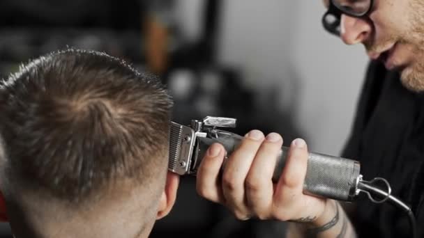 Tätowierte Friseur macht Haarschnitt für Kunden im Friseursalon mit Haarschneidemaschine, Herrenfriseur und Rasur beim Friseur, Friseur und Rasiersalon — Stockvideo