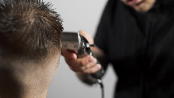 Barbeiro tatuado faz corte de cabelo para o cliente na barbearia usando hairclipper, corte de cabelo homem e barbear no cabeleireiro, barbearia e salão de barbear — Vídeo de Stock