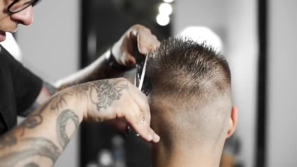 Peluquero tatuado hace corte de pelo para el cliente en la peluquería mediante el uso de tijeras y peine, corte de pelo mans y afeitado en la peluquería, peluquería y salón de afeitado — Vídeos de Stock