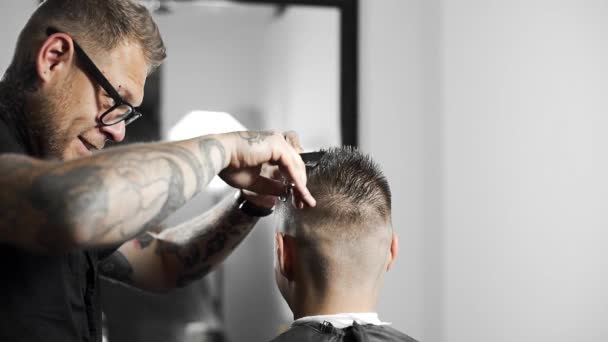 Peluquero tatuado hace corte de pelo para el cliente en la peluquería mediante el uso de tijeras y peine, corte de pelo mans y afeitado en la peluquería, peluquería y salón de afeitado — Vídeos de Stock