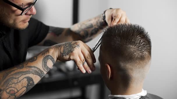 Peluquero tatuado hace corte de pelo para el cliente en la peluquería mediante el uso de tijeras y peine, corte de pelo mans y afeitado en la peluquería, peluquería y salón de afeitado — Vídeos de Stock