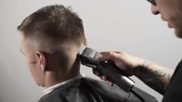 Tattoed barbiere rende taglio di capelli per il cliente presso il negozio di barbiere utilizzando tagliacapelli, taglio di capelli mans e rasatura presso il parrucchiere, barbiere e salone da barba — Video Stock