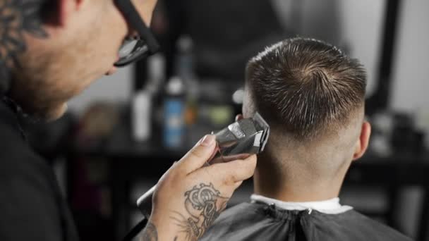 Peluquero tatuado hace corte de pelo para el cliente en la peluquería mediante el uso de peluquero, corte de pelo mans y afeitarse en la peluquería, peluquería y salón de afeitar — Vídeos de Stock