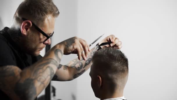 Peluquero tatuado hace corte de pelo para el cliente en la peluquería mediante el uso de tijeras y peine, corte de pelo mans y afeitado en la peluquería, peluquería y salón de afeitado — Vídeos de Stock