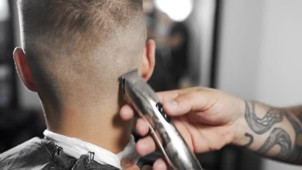 Tattoed barber makes haircut for customer at the barber shop by using hairclipper, mans haircut and shaving at the hairdresser, barber shop and shaving salon — Stock Video