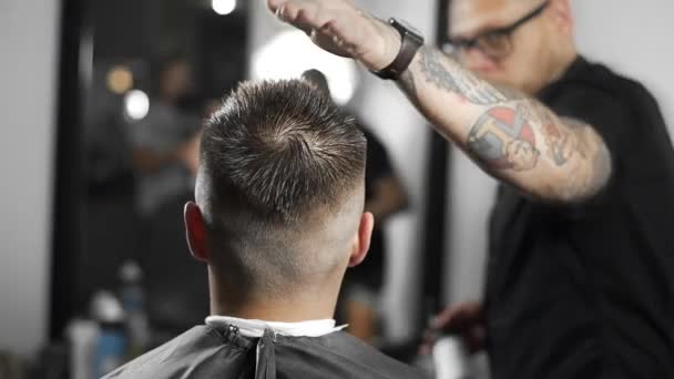Peluquero tatuado hace corte de pelo para el cliente en la peluquería, corte de pelo mans y afeitado en la peluquería, peluquero termina el corte de pelo para el cliente — Vídeo de stock