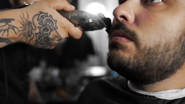 Peluquería tatuada cizalla la barba de los clientes mediante el uso de trimmer en la peluquería, corte de pelo mans y afeitarse en la peluquería, peluquería y salón de afeitar — Vídeos de Stock