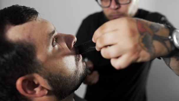 Tattoed Kapper shears de klanten mustage met behulp van de tondeuse en kam op de kapper, mans kapsel en scheren bij de kapper, Kapper en scheren salon — Stockvideo