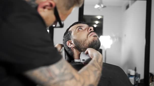 Barbeiro tatuado tosquia a barba dos clientes usando aparador na barbearia, corte de cabelo homem e barbear no cabeleireiro, barbearia e salão de barbear — Vídeo de Stock