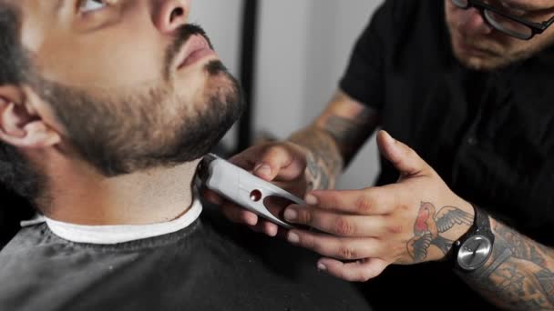 Tatoveret barber saks kunderne skæg ved hjælp af trimmer på barber butikken, mans frisure og barbering på frisør, frisør butik og barbersalon – Stock-video