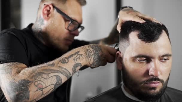 Парикмахер Tattoed делает стрижку для клиента в парикмахерской с помощью стрижки, стрижки и бритья в парикмахерской, парикмахерской и салоне бритья — стоковое видео