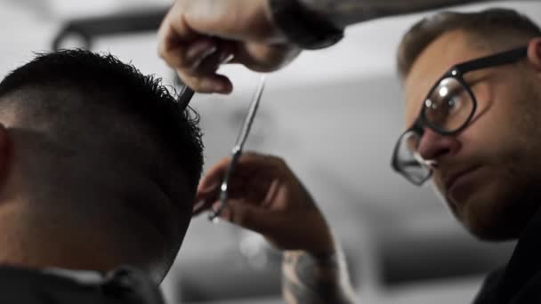 Tattoed barber makes haircut for customer at the barber shop by using scissors and comb , mans haircut and shaving at the hairdresser, barber shop and shaving salon — Stock Video